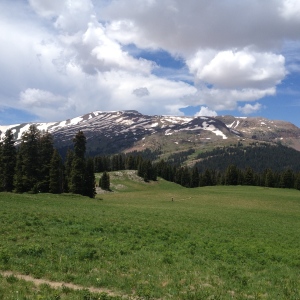 Snowy mountains in Crested Butte in July, seen from 401 with riders on the trail below.